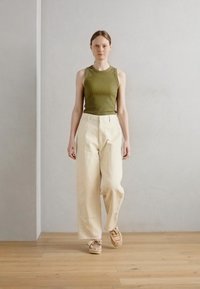 Débardeur côtelé olive, pantalon large crème, et baskets beiges. Textures lisses, design simple, contraste de couleurs subtil et coupe décontractée.
