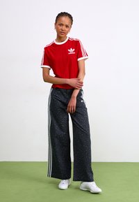 Piros és fehér csíkos adidas póló logóval, fekete mintás, bő szárú nadrággal párosítva, fehér oldalsó csíkokkal. Fehér sportcipő.