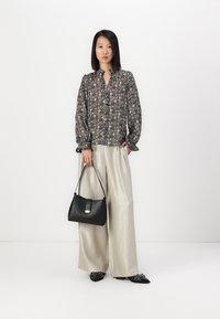 Μπλούζα με μακριά μανίκια από μαύρο και εμπριμέ ύφασμα, συνδυασμένη με ανοιχτόχρωμο, φαρδύ παντελόνι. Κρατάει μια μικρή μαύρη τσάντα χειρός με ασημένιο κούμπωμα.