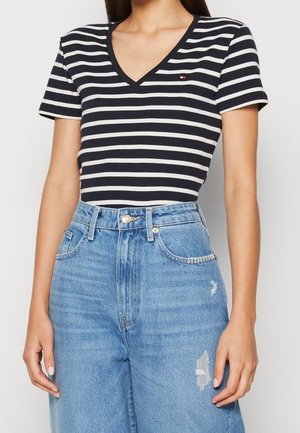 Kvinde iført en sort og hvid stribet V-hals kortærmet top indstukket i højtaljede blå jeans med let slid på låret.