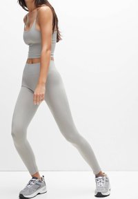 Débardeur de sport gris associé à un legging taille haute assorti ; texture lisse, design ajusté, complété par des baskets grises.