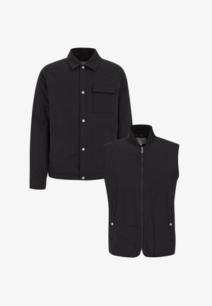 Svart vadderad jacka med tryckknappar och bröstficka, ihopparad med en ärmlös väst med dragkedja. Båda har en slät yta.