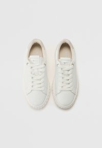 Paire de baskets basses blanches avec des semelles épaisses et des lacets blancs, vues de dessus sur un fond clair.