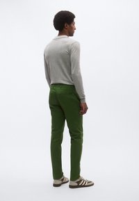 Ανοιχτό γκρι πόλο πουκάμισο με μακριά μανίκια, συνδυασμένο με πράσινο παντελόνι και καφέ αθλητικά παπούτσια με λευκές ρίγες. Λείο ύφασμα, εφαρμοστή σχεδίαση, κλασική σιλουέτα.