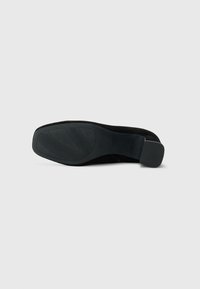 Black suede shoe featuring a smooth, structured upper and a textured rubber sole with a distinctive tread pattern. Clean lines and minimal design.