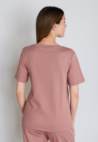 Lyhythihainen mauve t-paita, pehmeää puuvillakangasta, yksinkertainen design, pyöreä kaula-aukko, näkyvä ommel, nähty takaa sileällä pinnalla.