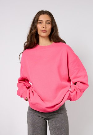 Rosafarbener, übergroßer Sweatshirt mit Rundhalsausschnitt und langen Ärmeln. Kombiniert mit figurbetonten, funkelnden grauen Leggings. Durchgängig glatte Textur.