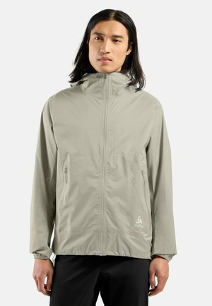 Veste légère à capuche de couleur gris clair, avec une texture douce, fermeture éclair intégrale et deux poches latérales. Logo dans le coin inférieur gauche.