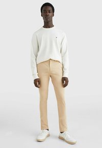 Maglione bianco a maglia, chinos beige e sneakers bianche. Le caratteristiche includono polsini a costine e un piccolo logo sul maglione, con una vestibilità dritta.