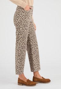 Beige wijde broek met panterprint in zwart en roestkleurige vlekken, voorzien van zijzakken en een hoge taille, gecombineerd met bruine loafers.