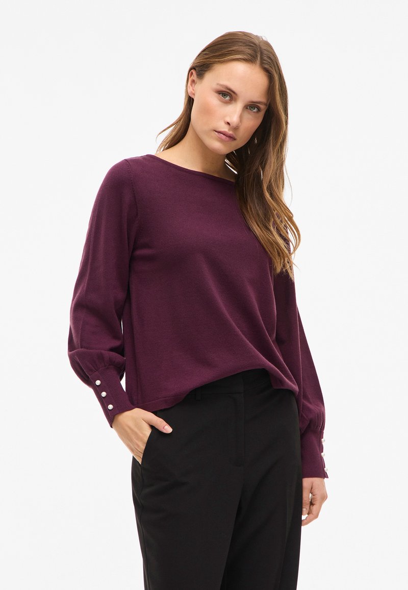 Paarse gebreide trui met lange mouwen, met knoopdetails bij de manchetten. Gecombineerd met een zwarte broek, ontworpen met een losse pasvorm.