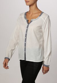 Camicia bianca a maniche lunghe con colletto grigio e chiusura a bottoni. Tessuto testurizzato con una vestibilità rilassata, caratterizzata da un orlo curvo e bottoni.