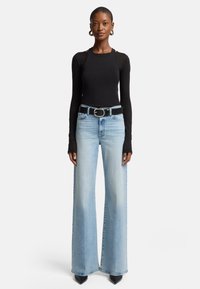 Zwarte lange mouw top, hoog-gesneden lichtblauwe wijde jeans, zwarte riem met zilveren gesp, puntige zwarte hakken. Glad textuur, casual pasvorm.