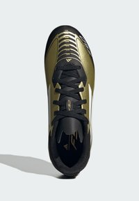 Zapatilla deportiva en dorado y negro con un diseño elegante, superficie texturada y un sistema de cordones destacado. Presenta un logo y una forma aerodinámica.
