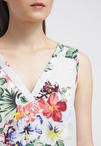 Mouwloze top met bloemenpatroon en V-hals, in de kleuren wit, groen, roze, rood en blauw. Soepele, lichte stof.