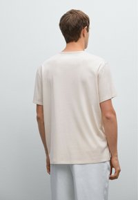 Light beige short-sleeve t-shirt made of soft fabric, featuring a crew neck, relaxed fit, and minimalistic design, displayed from the back.