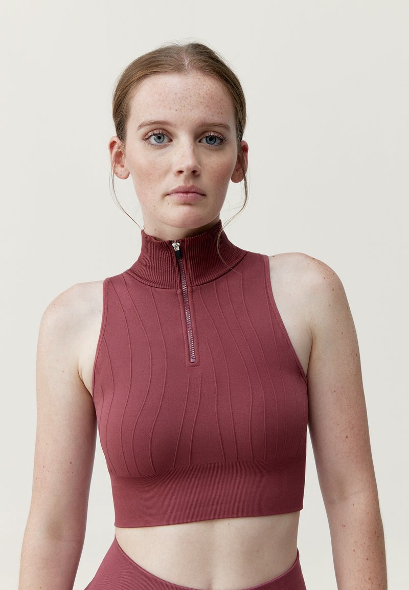 Bordová žebrovaná crop top s vysokým límcem a krátkým zipem. Má přiléhavý střih a texturovanou látku. Bez rozpoznatelných vzorů nebo akcentů.