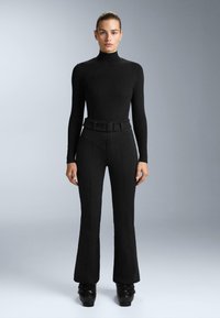 Hosszú ujjú fekete felső magas nyakkal, amelyhez magas derekú fekete trapéznadrág és textúrált öv tartozik. Fényes fekete platform cipők.