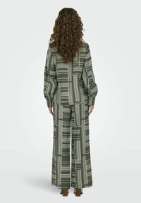 Abbigliamento verde a fantasia composto da un top e pantaloni larghi con linee bianche. Il materiale sembra leggero, con una texture sottile.