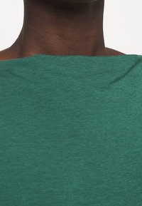 Groene, lichte top met een bootneck en een zachte textuur. Naadloos ontwerp met minimale stiksels en geen zichtbare hardware.