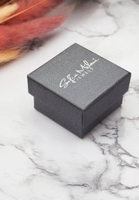 Svart strukturerad presentask med ett lock, prydd med vit text "Sofia Milani Jewels" på toppen. Positionerad på en marmorytan.