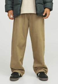 Beige, wijde broek gemaakt van zachte stof, met een gladde textuur en een licht geplooide uitstraling, gecombineerd met zwarte sneakers.