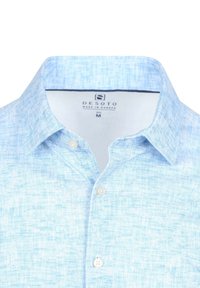 Lichtblauw blouse met een gestructureerde stof, korte kraag en twee witte knopen zichtbaar op de sluiting. Merkenlabel aan de binnenkant van de kraag.