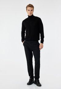 Czarny sweter z golfem wykonany z dzianiny, zestawiony z czarnymi spodniami slim-fit oraz czarnymi sneakersami na sznurowadła; gładka faktura i minimalistyczny design bez wzorów.