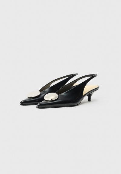 Czarne skórzane pantofle na obcasie typu slingback z ostrymi noskami, z dużym, okrągłym metalicznym akcentem na przodzie stopy i małym obcasem typu kitten.