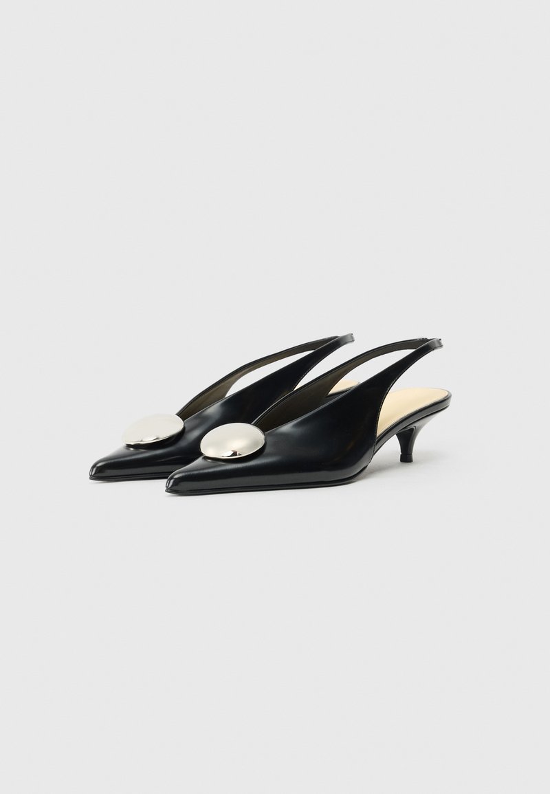Tacones slingback de cuero negro con punta afilada, que presentan un gran acento metálico redondo en el empeine y un pequeño tacón kitten.