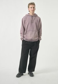 Verwaschene lavendelfarbene Kapuzenjacke mit Fronttasche und Kordelzug, kombiniert mit schwarzen weiten Hosen und schwarzen Sneakers. Einfaches und lässiges Design.