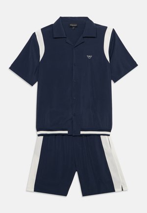 Navy blauwe korte mouw blouse met knopen en bijpassende korte broek met witte zijkanten en een klein logo op de borst van het shirt.
