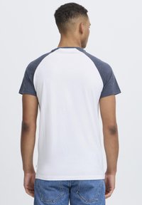 White t-shirt with navy raglan sleeves, cotton material, round neck, and a relaxed fit, displayed from the back with short sleeves.