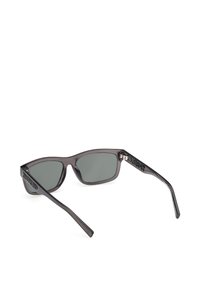 Lunettes de soleil rectangulaires gris foncé avec verres teintés et logo "Timberland" sur les branches, présentées en angle depuis l'arrière.