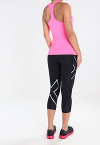 Rosa Sporttanktop und schwarze Capri-Leggings mit weißen Akzenten. Das Outfit hat eine figurbetonte Passform und besteht aus feuchtigkeitstransportierendem Material.