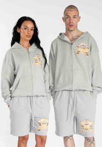 Felpe con cappuccio grigie con zip e pantaloni corti coordinati, entrambi con un design grafico arancione. Il tessuto sembra morbido con una vestibilità comoda.