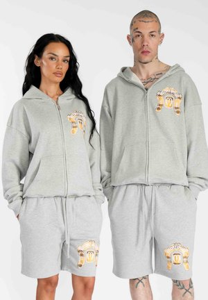Felpe con cappuccio grigie con zip e pantaloni corti coordinati, entrambi con un design grafico arancione. Il tessuto sembra morbido con una vestibilità comoda.