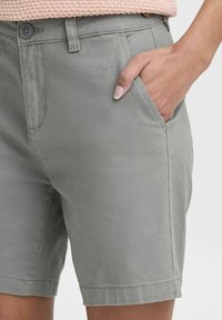 Pantalones cortos de algodón gris con una textura suave, presentan un bolsillo frontal, cierre de botón y un ajuste entallado. El dobladillo es recto y limpio.