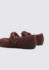 Brown fuzzy slippers made of textured material, featuring a buckle accent and a rounded shape, with a flat sole and open design.