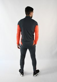 Conjunto atlético gris y naranja hecho de tejido elástico, que presenta un cuello con cremallera, mangas largas y pantalones ajustados con tobillos con cremallera.