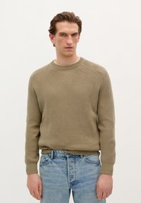 Beige ribbed knit sweater with a crew neckline, long sleeves, and a relaxed fit, paired with light blue denim jeans.