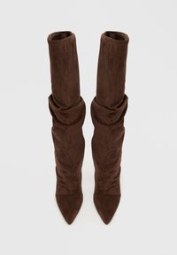 Καφέ μπότες από σουέτ πάνω από το γόνατο με χαλαρή σχεδίαση, μυτερή μύτη και απαλή υφή, με ελαφρώς ρυτιδιασμένο πάνω μέρος για επιπλέον λεπτομέρεια.