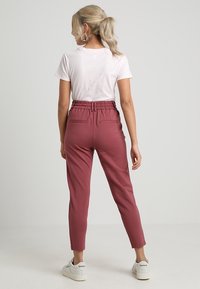 Bordeaux gekleurde tapered broek met een elastische tailleband en twee achterzakken, gecombineerd met een aansluitend wit T-shirt en witte sneakers.