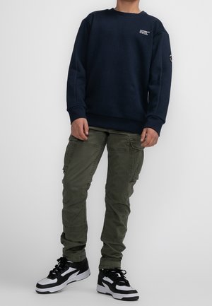 Laivastonsininen collegepaita pyöreällä pääntiellä, resoroiduilla hihansuuilla ja logodetaljilla. Oliivinvihreät cargo-housut, joissa on useita taskuja, sekä mustavalkoiset lenkkarit.