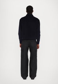 Navy corduroy jacket with a collared neck, paired with black cargo pants featuring multiple pockets. Solid color, relaxed fit.