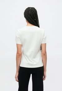 Λευκό κοντομάνικο T-shirt με στρογγυλή λαιμόκοψη, απαλό ύφασμα και μικρή λεπτομέρεια λογοτύπου στο πίσω μέρος. Συνδυασμένο με μαύρο τζιν.