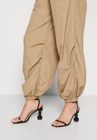 Beige, wijde broek gemaakt van lichtgewicht materiaal met elastische boorden, gecombineerd met zwarte sandalen met bandjes en ronde, getextureerde hakken.