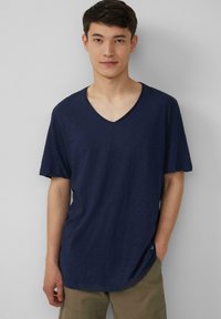 Granatowa koszulka z krótkim rękawem i dekoltem w kształcie litery V; wykonana z lekkiego materiału o gładkiej fakturze; wyróżnia się luźnym krojem i detalami w szwach bocznych.