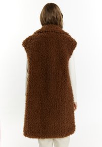 Brun faux fur vest med en blød, fluffy tekstur, ærmeløs design og sjal-krave, med en A-formet silhuet der når midt på låret.