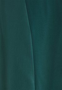 Gros plan de deux panneaux de tissu vert foncé adjacents avec des textures différentes et une couture visible entre eux.